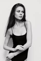 Fototapeta premium Beautiful young woman in a black bodysuit, posing gracefully against a plain white background. The image conveys elegance and self-confidence.