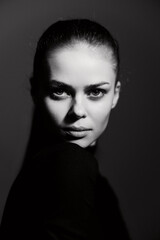 Confident woman with sleek hair gazing directly at the camera, dressed in a black outfit, captured in dramatic black and white lighting. Intense and striking portrait.