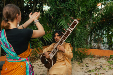 Indian musician in traditional clothes playing sitar festive season outdoor home. Smiling young...