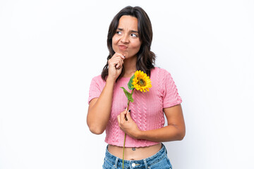 Young hispanic woman holding sunflower isolated on white background and looking up