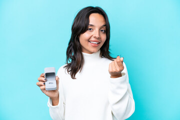 Fototapeta premium Young hispanic woman holding a engagement ring isolated on blue background making money gesture