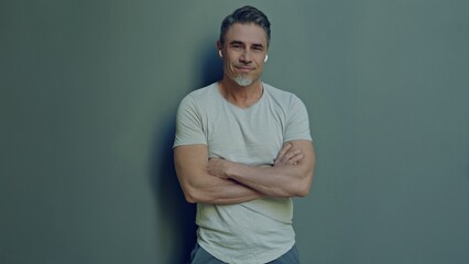 Portrait of a relaxed man in 50s, happy smile. Confident middle aged male arms crossed. Blank copy space for text on grey wall background.