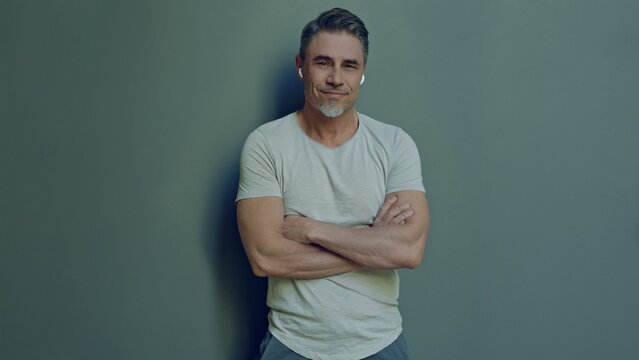 Portrait of a relaxed man in 50s, happy smile. Confident middle aged male arms crossed. Blank copy space for text on grey wall background.