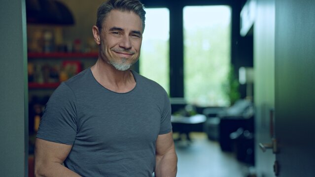 Portrait of smiling man in 50s, relaxed and confident smile, dressed in casual grey t-shirt in modern home interior. Happy mid adult, middle aged male looking at camera. - Powered by Adobe