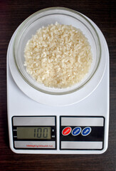 Plate with rice on top on kitchen scale 100 grams. Rice porridge in glass bowl isolated on black background with clipping path, top view