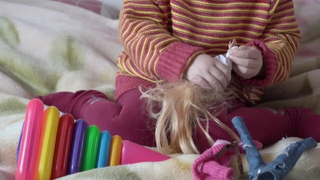 little girl undresses doll, child on bed playing with doll, undressing doll's clothes