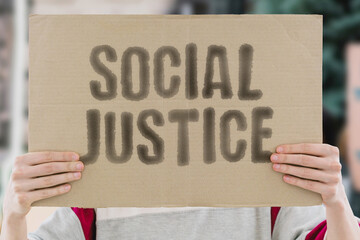 The phrase 'Social Justice' on a banner in a person's hand. Human holds a cardboard with an inscription. Equality. Fairness. Rights. Humanity. Inclusion. Change. Advocacy