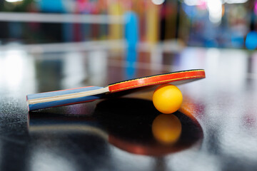 Racket and a ping pong ball are lying on the table in close-up.