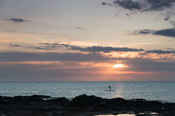 Silhouette of man paddling a sup in a calm sunset.