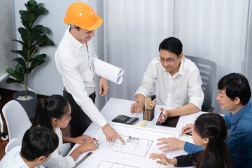 Diverse group of civil engineer and client working together on architectural project, reviewing construction plan and building blueprint at meeting table. Prudent