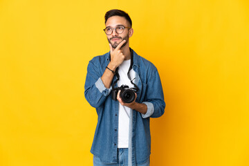 Young photographer girl isolated on yellow background having doubts