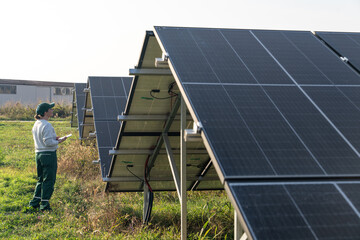 Female farmer with digital tablet on a modern farm using solar panels. Agricultural silos in the...