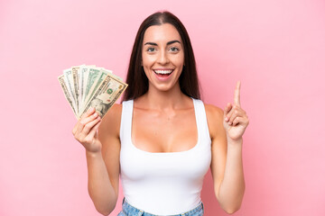 Young caucasian woman taking a lot of money isolated on pink background pointing up a great idea