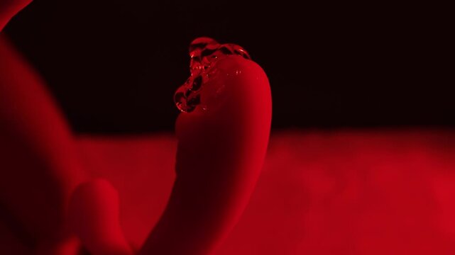 A woman holds adult toys and a condom in her hand on a white blanket in a bedroom.
