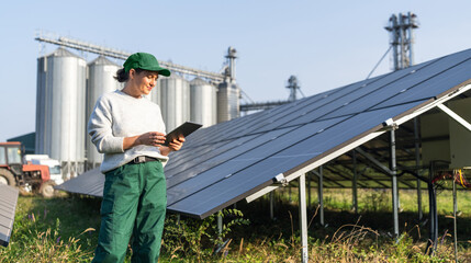 Female farmer with digital tablet on a modern farm using solar panels. Agricultural silos in the background. © scharfsinn86