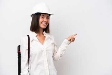 Young architect woman with helmet and holding blueprints isolated on white background pointing finger to the side