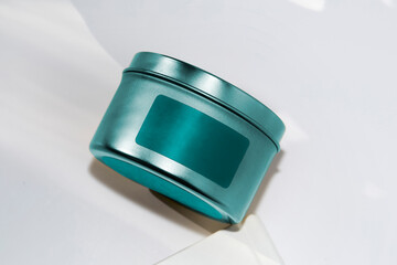 Luxury candle in a colorful tin with a blank label. Photograph with a white background and space for copy. Teal design.