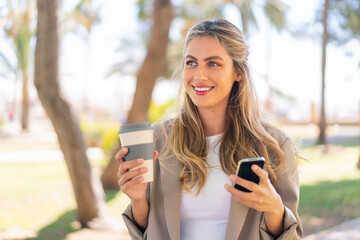 Young pretty blonde Uruguayan woman at outdoors using mobile phone and holding a take away coffee