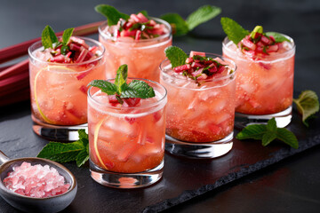 National Rhubard Vodka Day. A collection of sparkling rhubarb drinks served in glasses with mint garnish, enhanced with vibrant red tones and natural light on a dark slate surface.
