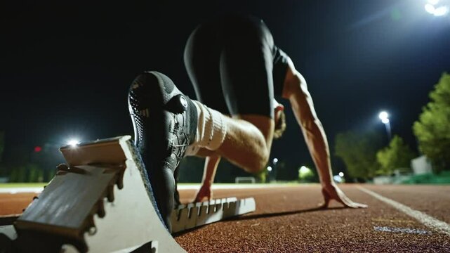 Strong Young Man Starting a Race From Track Starting Blocks Position on a Dark Stadium in the Evening. Cinematic Portrait of a Fit Male Sprint Runner Participating in a Competition