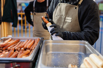 Man cooks hot sausages in a bun at a street festival, a fair.