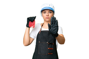 Butcher woman wearing an apron and serving fresh cut meat over isolated chroma key background making stop gesture