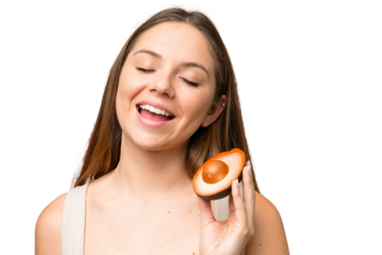 Young blonde woman over isolated chroma key background holding an avocado while smiling. Close up portrait