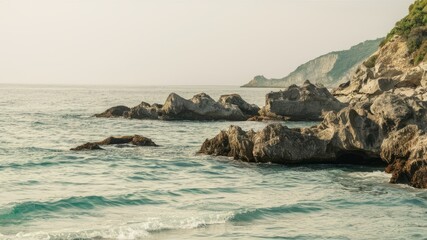 Fototapeta premium Coastal Serenity: The tranquil scene captures the rugged beauty of a rocky coastline, where the gentle sea meets the shore under a clear, overcast sky, conveying a sense of peace and natural elegance.
