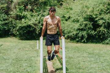 Fit man exercising in nature, performing triceps dips on parallel bars in a lush green park