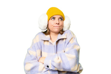 Young blonde woman wearing winter muffs over isolated chroma key background making doubts gesture...
