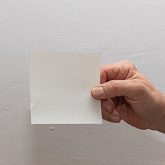 Obraz premium Hand holding a blank white paper on a plain background, ideal for messages
