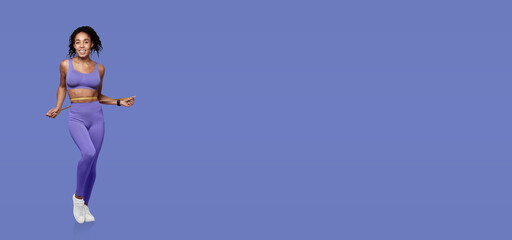 A woman is engaged in a joyful exercise routine, wearing purple activewear that complements her energetic movements. The bright blue background enhances her vibrant appearance.