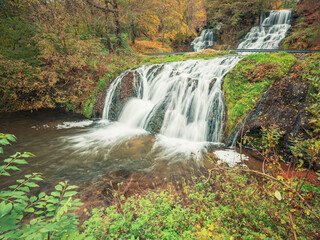 view to huge waterfall with cascades in autumn forest