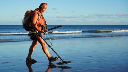 Senior gold digger with metal detector on shore searching for lost coins and jewelry
