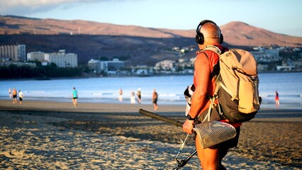 Gold Digger. Senior treasure hunter searching for jewels with metal detector on the beach of tourist resort