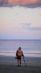 Gold prospector. Senior treasure hunter searching for jewels and coins with metal detector on beach and enjoying seascape