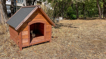 A wooden doghouse placed in a dry park area surrounded by trees, ideal for concepts of pet care, outdoor living, or sustainable animal sheltering, with potential for pet product advertisements.