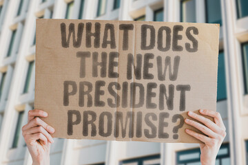 The phrase 'What does the new president promise?' on a banner in a person's hand. Human holds a cardboard with an inscription. Leadership. Vision. Change. Governance. Policy. Future. Hop