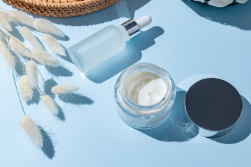 Minimalist skincare packaging with jar and dropper bottle on blue background