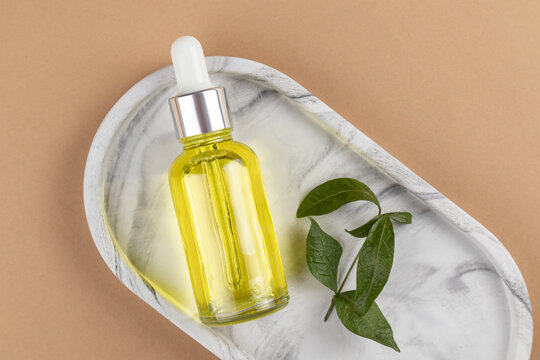 Elegant cosmetic dropper bottle on marble tray with leaf