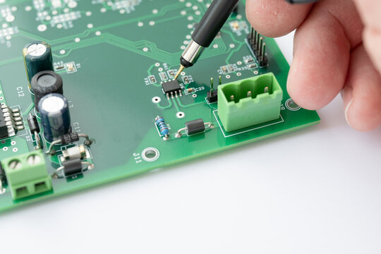 Hand Testing Microchip on Green Circuit Board
