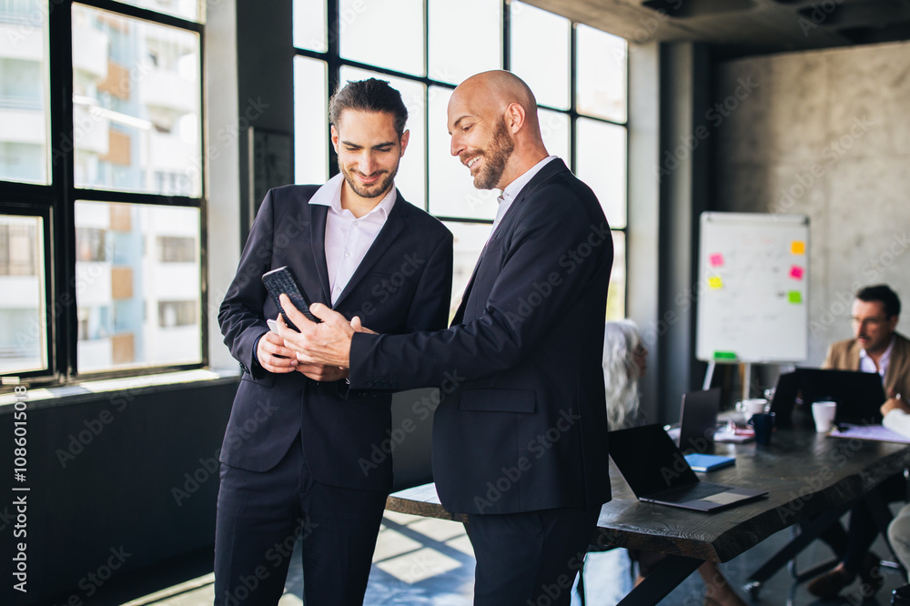 Aufkleber two men in suits review documents on a device while collaborating in a stylish office. natural light