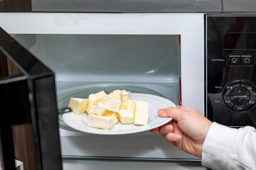 Close-up of female hand melting butter in microwave oven on white plate. Stage of cooking pie.
