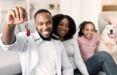 New Homeowners Concept. Happy black man, woman, girl and dog celebrating relocation, father holding and showing key of their apartment house, selective focus, blurred background