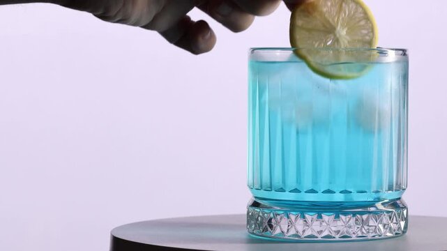 Lemon added to blue cocktail on white background