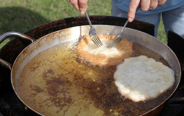 two fried fritters in a pot of boiling oil and the cook turning them with steel forks during a...