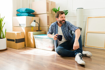 Man happily sipping coffee and unwinding on the floor of his new apartment amidst moving boxes