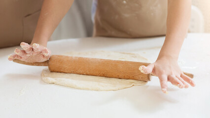 Granny's baking class. Unrecognizable child rolling dough with grandmother at table, closeup of hands