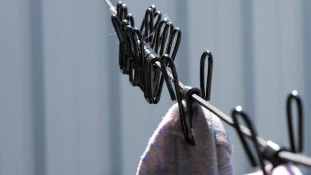 Laundry clothespins attached to the laundry rope sway slowly outdoors. Black metal clothespins hanging on the clothesline string.
