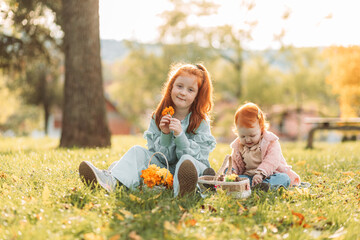 Two ginger, redhead little girls sitting outdoors in the park, playing